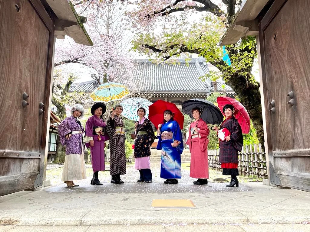 桜の咲く寺院の門前で着物姿の参加者たちが並ぶ様子